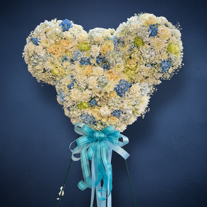Shaped arrangement of flowers with a blue ribbon on a dark wooden background